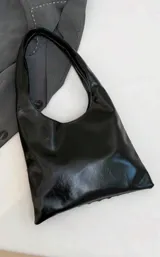 Cartera tipo hobo de color negro con acabado brillante, decorada completamente con remaches metálicos circulares de diversos tamaños.