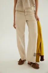 Pantalón de corte recto y tiro medio con costuras a la vista, bolsillos delanteros y traseros, y un detalle de pin de la marca en el ruedo.
