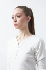 Remera de manga larga color beige, confeccionada en algodón, con escote en V y cartera corta de botones blancos.