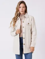 Sobrecamisa de corte amplio confeccionada en tejido suave al tacto, color beige. Presenta cuello de solapa, cierre frontal con botones efecto carey, dos bolsillos frontales con solapa y mangas largas con puños abotonados. El ruedo es redondeado en los laterales y cuenta con canesú en la espalda.