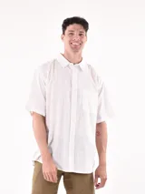 Camisa de manga corta color blanco roto con textura de tejido de lino o similar, corte holgado y cuello camisero.