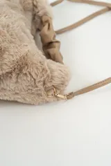 Cartera de mano confeccionada en piel sintética de textura suave y peluda, color beige. Presenta un asa superior fruncida de material liso y una correa larga ajustable y extraíble con herrajes metálicos dorados.