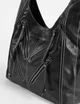 Cartera hobo negra de cuero sintético con costuras blancas decorativas y múltiples cierres diagonales en el frente. Tiene una correa de hombro ajustable.