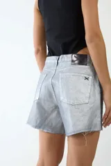 Short de jean color gris plateado con apliques metálicos y ruedo desflecado.