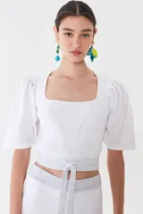 Top blanco tejido en hilado liviano con escote recto y mangas balloon de poplín 100% algodón. Tiene tiras tejidas para ajustar en la cintura.