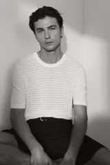 Remera de punto color blanco, con textura de pequeños patrones en relieve, cuello redondo y mangas cortas.