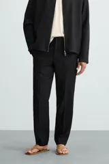 Pantalón negro de corte regular fit, confeccionado en tejido de lino. Presenta cintura con botón y cierre de cremallera, bolsillos frontales y bolsillos traseros de doble vivo.