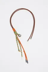 Colgante para bolso con cordones de cuero marrón, cordones trenzados naranja y verde, y dije metálico plateado.