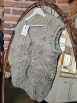 Chaleco tejido a mano color gris claro, con cuello en V y diseño trenzado.