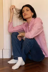 Camisa de corte clásico con estampado de rayas verticales rojas y blancas, cuello camisero con volados y cierre frontal de botones.