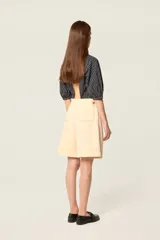 Bermuda de tiro alto en color crudo, confeccionada en lona de algodón. Presenta un corte acampanado con pliegues en la cintura, bolsillos delanteros inclinados y costuras decorativas en contraste color camel.
