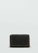 Bolso tipo sobre de fibra natural tejida en color negro, con detalle de tachuelas metálicas doradas en el borde. Cuenta con cierre de solapa con botón magnético, forro interior y asa larga de cadena metálica dorada.