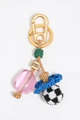 Llavero de la marca Bimba y Lola confeccionado con cordón trenzado y diversos charms. Incluye un mosquetón y aro metálicos en tono dorado, una pieza de resina rosada, un detalle de rafia azul, una cuenta con diseño damero en blanco y negro, y un cubo metálico con el logo grabado.