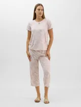 Pijama de dos piezas en tono rosado con estampado floral, compuesto por una remera de manga corta con escote redondo y detalle de gota con botón, y un pantalón capri con cintura elastizada.