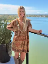 Vestido midi de terciopelo con estampado en tonos tierra y verdes. Presenta un corte holgado, mangas cortas y un escote en V destacado por un aplique artesanal de cuero en tonos verdes y marrones, unido con bordados a mano.