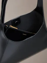 Cartera mediana Calvin Klein de poliuretano color negro, diseño estructurado tipo hobo, con correa de hombro ajustable y detalles metálicos dorados.
