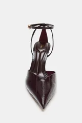 Zapato destalonado de tacón alto fino con acabado efecto acharolado. Presenta un diseño de punta fina y cierre mediante tira con hebilla ajustable al tobillo.