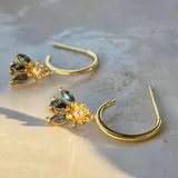 Par de aros dorados tipo argolla con dije colgante de cristal facetado con forma de hoja y circonita redonda.