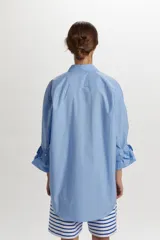 Camisa azul celeste de algodón, con corte oversize y diseño asimétrico en el ruedo. Cuenta con cuello camisero, cierre frontal con botones y mangas largas con puños estructurados y detalle fruncido.
