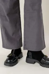 Bota corta de cuero negro con suela track, cierre frontal con cremallera y tira decorativa con hebilla metálica sobre el empeine.