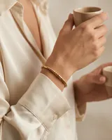 Pulsera esclava de acero con baño de oro, compuesta por una secuencia de cuentas esféricas y cilíndricas pequeñas.