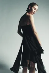 Vestido midi negro, con escote pico adornado con encaje a tono y tirantes finos. Presenta una cascada de volantes en la parte delantera y un bajo asimétrico.