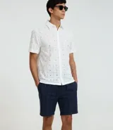 Bermuda recta de playa en color blanco roto, confeccionada en algodón texturizado con efecto de rayas verticales. Posee cintura elástica con cordón ajustable.