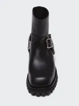 Bota corta de cuero negro con punta cuadrada, suela track y detalle de estribo desmontable con hebilla metálica.