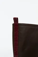Bota de cuero color chocolate, de caña alta y suela track. Presenta detalle de textura símil cocodrilo en la parte trasera de la caña.