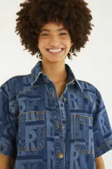 Camisa de jean de manga corta con calce recto, cuello clásico, bolsillos frontales con solapa y cierre de botones metálicos. Presenta un estampado gráfico con monograma en tonos de azul.