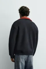 Chaqueta relaxed fit de color negro, confeccionada en tejido de canalé con mezcla de lana. Presenta cuello redondo, puños y dobladillo en rib elástico, bolsillos frontales de vivo y cierre con botones a presión.