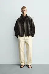 Cazadora bomber de corte relajado confeccionada en piel. Presenta cuello subido, manga larga ranglán, bolsillos de vivo en la cadera y bajo con elástico. Cierre frontal con cremallera oculta por solapa con botones a presión.