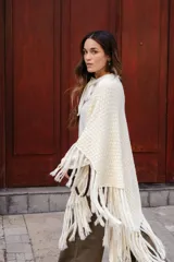 Poncho triangular de lana en color crudo, con diseño de tejido texturizado y terminaciones de flecos largos en todo el borde.