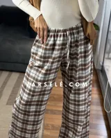 Pantalón tipo palazo de corte amplio y tiro alto, confeccionado en tela con estampado de cuadros escoceses en tonos marrones, blancos y negros. Cuenta con cintura elástica y bolsillos laterales.