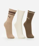 Kit de tres pares de medias deportivas Puma de caña larga. Un par es beige con dos rayas marrones y logo de Puma. Otro par es blanco liso. El tercer par es marrón oscuro con dos rayas blancas y logo de Puma. Todas están confeccionadas en algodón.