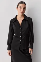 Camisa blanca de manga larga con textura suave y caída liviana, cuello camisero, puños anchos y fruncidos sutiles en los hombros.