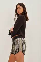 Short de tiro medio con diseño de rayas verticales en lentejuelas plateadas, doradas y negras. Presenta un corte ajustado con bordes redondeados y ribete negro en el ruedo.
