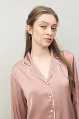 Camisa de pijama color rosado, de silueta clásica y tacto sedoso. Confeccionada en tejido satinado con leve elasticidad, presenta cuello camisero, cierre frontal con botones y detalles de vivo blanco que realzan el diseño.