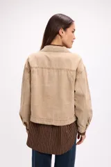 Campera de denim en tono beige, de corte cropped, con cuello camisero, cierre frontal con botones metálicos y bolsillos frontales tipo parche.