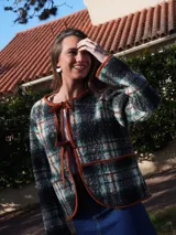 Saco abrigado de tejido texturizado en tonos marrones y negros, con diseño a cuadros, ribetes de lino en los bordes y cierre frontal con lazos.