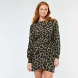 Vestido corto de manga larga con estampado de leopardo en tonos verde caqui y negro. Presenta un diseño con cuello redondo y un detalle drapeado con nudo lateral en la cintura que crea un efecto cruzado en la falda.