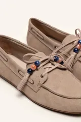Mocasín estilo náutico de gamuza marrón, con cordones de cuero, borla decorativa y cuentas de colores en el empeine.