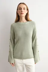 Sweater de punto color blanco natural, con cuello redondo y mangas largas adornadas con botones dorados a lo largo de las costuras exteriores.