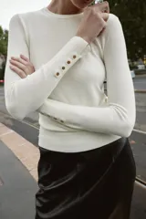Jersey de punto liso con cuello redondo y manga larga. Presenta detalle de botones decorativos en los puños.