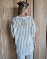 Remerón de tejido de punto calado en color arena, con cuello en V con terminación festoneada y mangas cortas amplias.