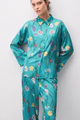 Pijama de satén turquesa con estampado floral multicolor, compuesto por una camisa de manga larga con botones y cuello camisero, y pantalón largo a juego.
