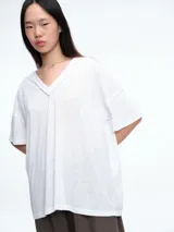 Remera de corte holgado y silueta cómoda, con escote en V y mangas cortas. Presenta costuras visibles en el cuello y los hombros, con un diseño minimalista y versátil.
