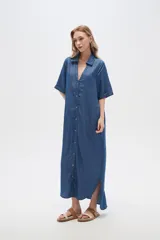 Vestido largo tipo camisero de lyocell, con cuello camisero, cierre frontal de botones, mangas cortas con dobladillo y bolsillos laterales. Presenta un corte holgado y tajos laterales en el ruedo.