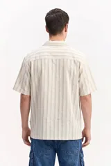 Camisa de manga corta oversize en tejido rústico, con diseño de rayas verticales celestes y blancas, cuello clásico y cierre frontal de botones.