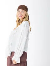 Blusa color blanco confeccionada en bambula liviana, con textura suave y caída fluida, escote en V con volados y mangas largas con puños elásticos.